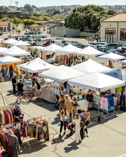 Wide angle on an outdoor market with a series of booths where retailers are selling products.